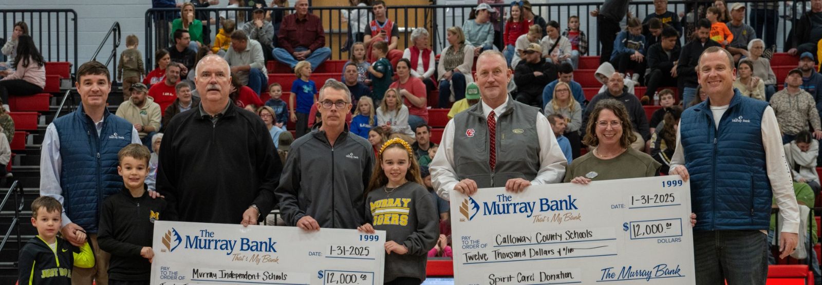 People holding large checks and debit card images in school gym.